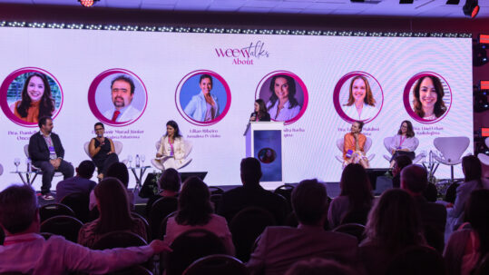Palco weeTalks com seis especialistas no telão e quatro painelistas debatendo perante a plateia.
