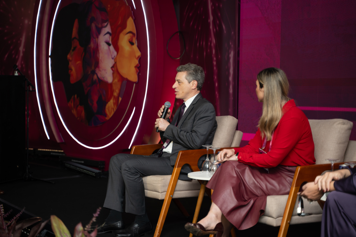 Participante fala ao microfone durante um painel, enquanto outra participante acompanha a discussão sentada ao lado.