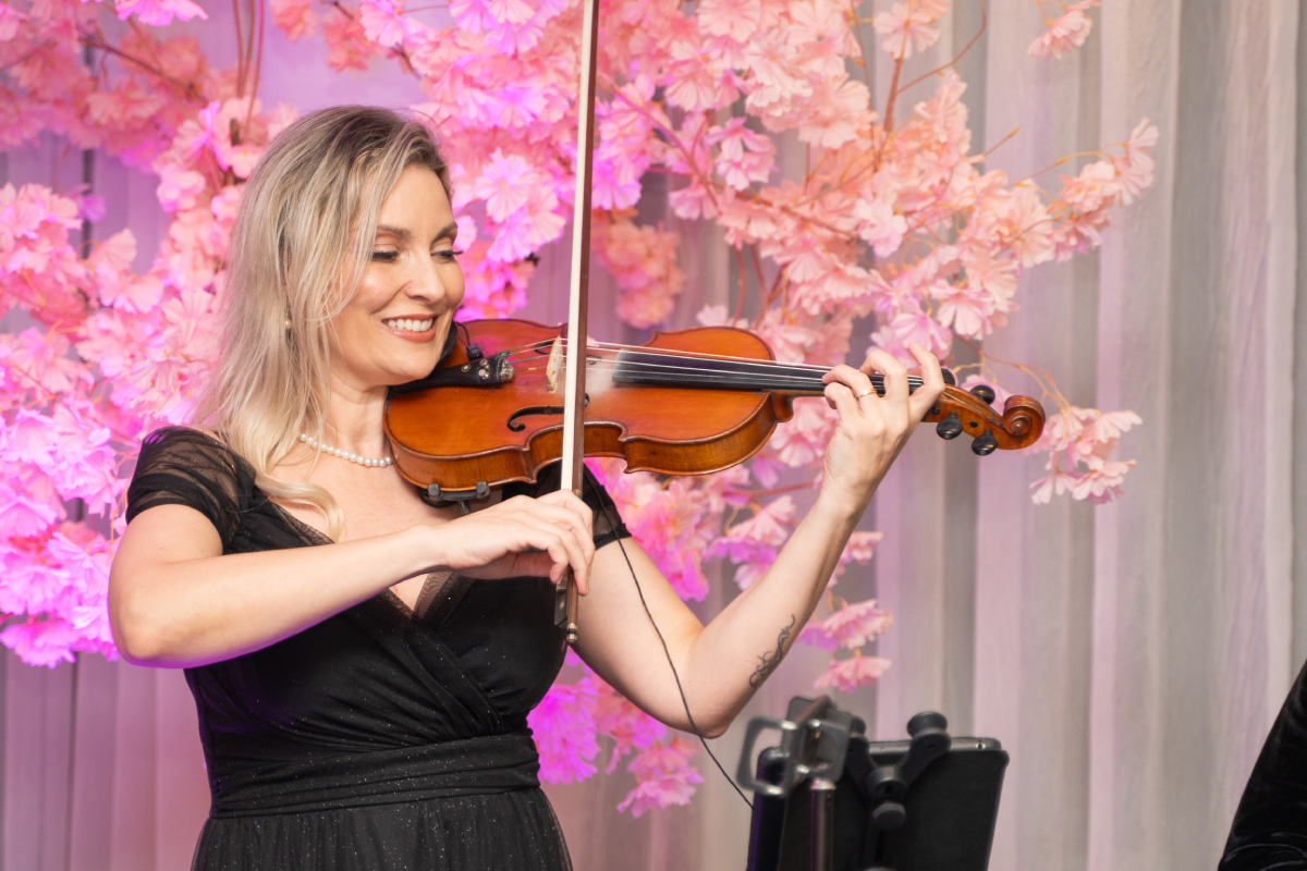 Violinista toca durante uma apresentação musical em ambiente decorado com flores cor-de-rosa.
