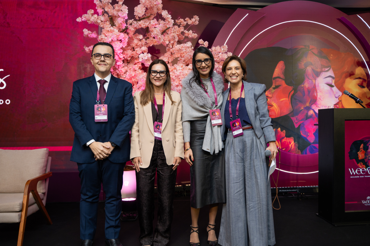 Quatro participantes posam juntas no palco do WEEM Talks 2026, diante da decoração com flores cor-de-rosa.
